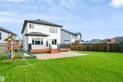 Spacious rear yard featuring a wooden privacy fence, a large deck with black railings, a paved patio area, and a bright green lawn - 