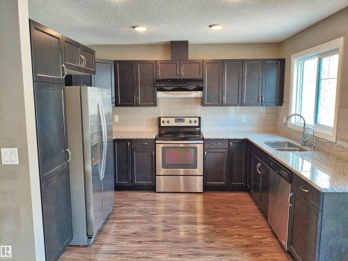 U-shaped kitchen featuring dark wood cabinetry, stainless steel appliances, granite-look countertops, and a subway tile backsplash - 23 1508 105 Street, Edmonton, AB 