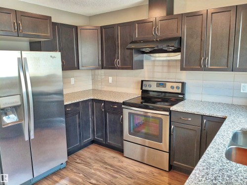 Kitchen featuring dark wood-finish cabinetry, speckled countertops, and a full suite of stainless steel appliances - 23 1508 105 Street, Edmonton, AB 