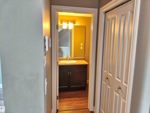 Bathroom entrance featuring a dark wood-finish vanity with a light countertop, a vessel sink, and a wall-mounted light fixture above a mirror - 23 1508 105 Street, Edmonton, AB 