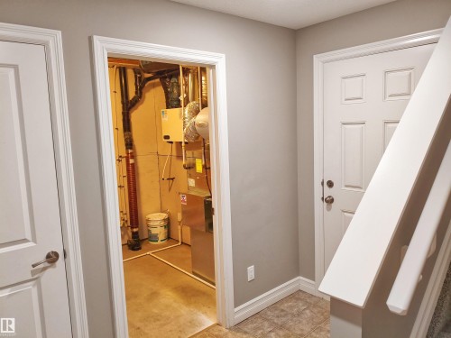 Interior hallway featuring a tile flooring, a white paneled door, and a staircase with white balusters - 23 1508 105 Street, Edmonton, AB 