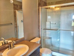 Bathroom featuring a glass-enclosed shower with a built-in shelf, an additional shower/tub combination, a vanity with an integrated sink, and an exhaust fan - 