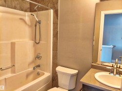Bathroom featuring a bathtub with an integrated shower, tiled shower surround, toilet, and a vanity with an integrated sink and mirror - 
