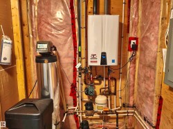 Utility space featuring a tankless water heater, water softener system, and exposed plumbing - 