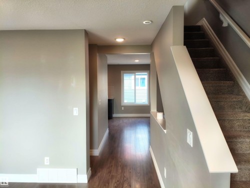 Entryway featuring neutral wall tones, recessed lighting, wood-finish flooring, white trim, and a carpeted staircase with a white railing - 23 1508 105 Street, Edmonton, AB 