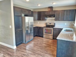Kitchen featuring dark wood-finish cabinetry, stainless steel appliances, speckled stone countertops, a tile backsplash, and wood-finish flooring - 