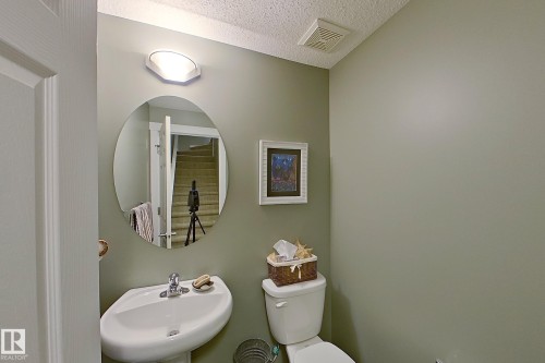 Pedestal sink with chrome faucet, oval mirror, and wall-mounted light fixture - 14412 98 Street, Edmonton, AB - Indoor Photo Showing Bathroom