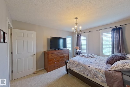 Bedroom featuring textured carpet flooring, a multi-paneled interior door, and a chandelier light fixture - 14412 98 Street, Edmonton, AB - Indoor Photo Showing Bedroom