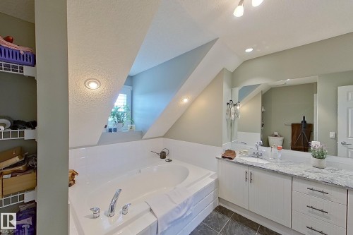 Spacious bathroom featuring a built-in soaking tub, a vanity with a light-colored countertop and white cabinetry, a large mirrored wall, recessed lighting, and tiled flooring - 14412 98 Street, Edmonton, AB - Indoor Photo Showing Bathroom