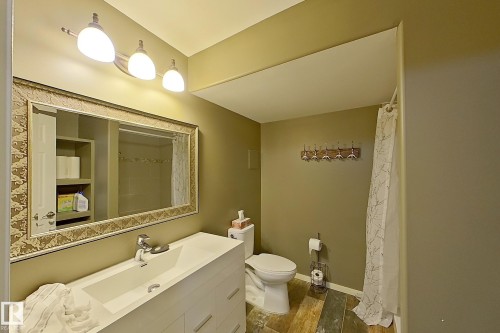 Bathroom featuring a vanity with an integrated sink, a framed mirror, and wood-finish flooring - 14412 98 Street, Edmonton, AB - Indoor Photo Showing Bathroom