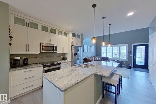 Modern kitchen featuring stainless steel appliances, light-toned cabinetry with frosted glass accents, and a large island with a dual-basin sink - 14412 98 Street, Edmonton, AB - Indoor Photo Showing Kitchen With Double Sink With Upgraded Kitchen