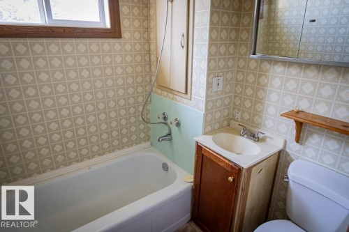 Bathroom featuring a white bathtub, patterned wall covering, wood-finish vanity with an integrated sink, and an overhead medicine cabinet - 5218 52 Ave, St. Paul Town, AB - Indoor Photo Showing Bathroom