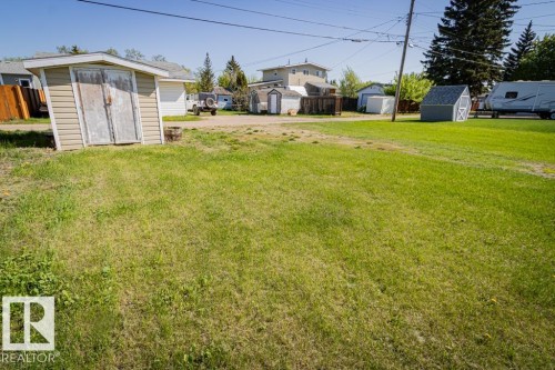Expansive grassy area with visible outbuildings and mature trees in the background - 5218 52 Ave, St. Paul Town, AB - Outdoor
