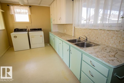 Utility room featuring a double basin sink, ample countertop space, upper and lower cabinetry, and two windows providing natural illumination - 5218 52 Ave, St. Paul Town, AB - Indoor Photo Showing Other Room
