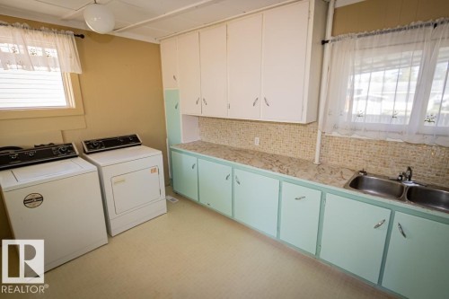 Utility room featuring a dual basin sink, laminate countertops, and ample cabinetry - 5218 52 Ave, St. Paul Town, AB - Indoor Photo Showing Laundry Room