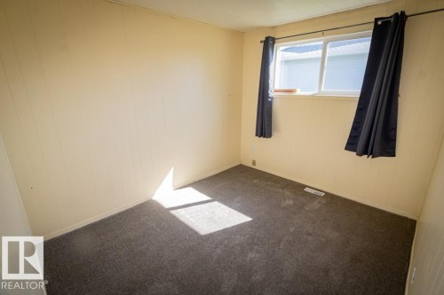 Room featuring neutral-toned vertical paneling, dark gray carpeting, and a white-framed window - 5218 52 Ave, St. Paul Town, AB - Indoor Photo Showing Other Room
