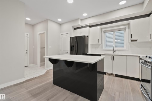 Kitchen featuring a central island with white countertop, white cabinetry with dark trim, black refrigerator, and built-in stainless steel range - 383 Charlesworth Drive, Edmonton, AB 
