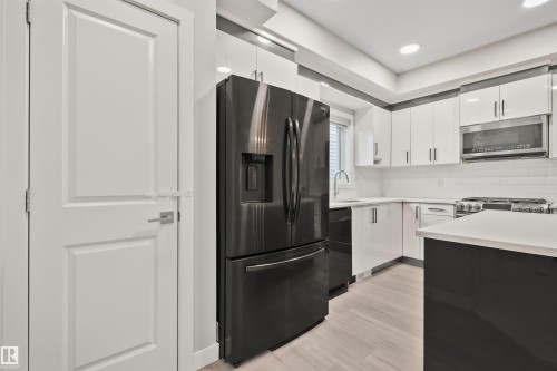 Modern kitchen featuring black stainless steel appliances, white subway tile backsplash, light wood-finish flooring, white upper cabinetry, and a contrasting dark kitchen island with a light countertop - 383 Charlesworth Drive, Edmonton, AB 