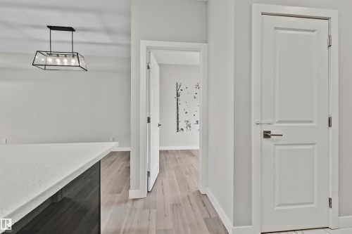 Kitchen island with a light-toned countertop, modern linear chandelier, light wood-finish flooring, white walls, and white interior doors - 383 Charlesworth Drive, Edmonton, AB 