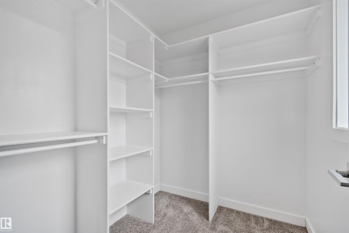 Walk-in closet featuring built-in shelving, multiple hanging rods, white walls, and gray carpet flooring - 383 Charlesworth Drive, Edmonton, AB 