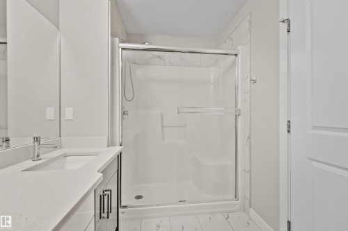Glass-enclosed shower with a built-in seat and marble-patterned tile surround - 383 Charlesworth Drive, Edmonton, AB 