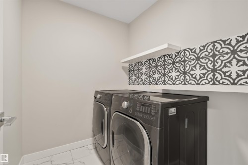 Laundry area featuring patterned wall tile, two floating shelves, and white floor tile - 383 Charlesworth Drive, Edmonton, AB 