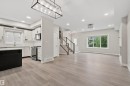 Open-concept living space featuring wood-finish flooring, a contemporary kitchen with stainless steel appliances, a kitchen island with seating, recessed lighting, and a prominent staircase with wood railings - 383 Charlesworth Drive, Edmonton, AB 
