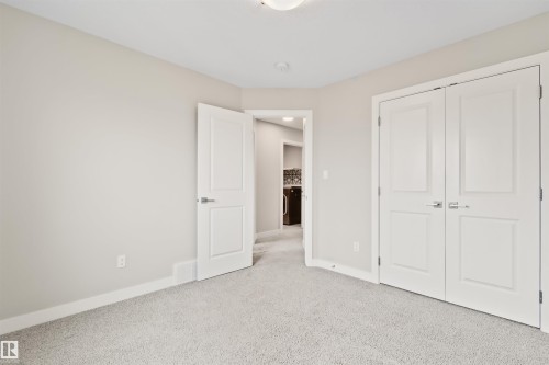 Carpeted room featuring a white paneled door, a double-door closet with polished chrome hardware, and light neutral wall paint - 383 Charlesworth Drive, Edmonton, AB 