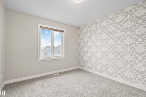 Room featuring a decorative accent wall with a floral pattern, neutral-toned carpeting, and a window with white trim - 383 Charlesworth Drive, Edmonton, AB 