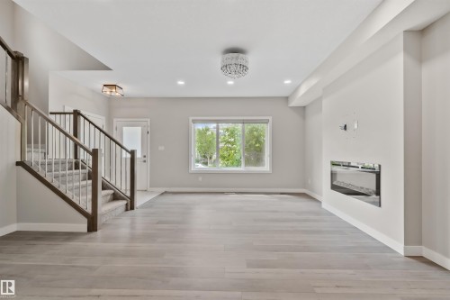 Open-concept living area featuring wood-finish flooring, a built-in electric fireplace, recessed lighting, a modern chandelier, and a carpeted staircase with wood railings - 383 Charlesworth Drive, Edmonton, AB 