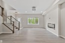 Open-concept living area featuring wood-finish flooring, a built-in electric fireplace, recessed lighting, a modern chandelier, and a carpeted staircase with wood railings - 383 Charlesworth Drive, Edmonton, AB 