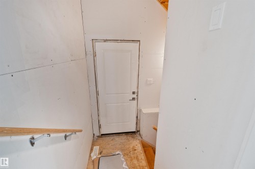 Interior space showcasing unfinished drywall, a paneled door with hardware, and exposed wood framing - 383 Charlesworth Drive, Edmonton, AB 
