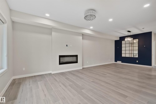 Open-concept interior featuring light wood-finish flooring, a contemporary linear fireplace, recessed lighting, a decorative crystal chandelier, and an accent wall with a modern mirrored fixture - 383 Charlesworth Drive, Edmonton, AB 