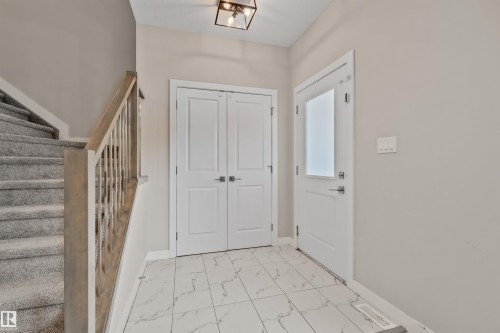Entryway featuring large format white tile flooring with dark veining, a light wood-finish staircase with carpeted treads, and a modern ceiling fixture - 383 Charlesworth Drive, Edmonton, AB 