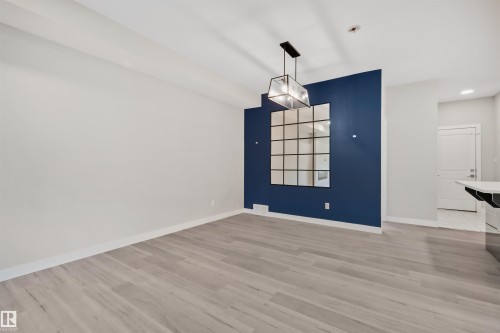 Open-concept living area featuring a prominent accent wall, wood-finish flooring, and a modern geometric pendant light fixture - 383 Charlesworth Drive, Edmonton, AB 