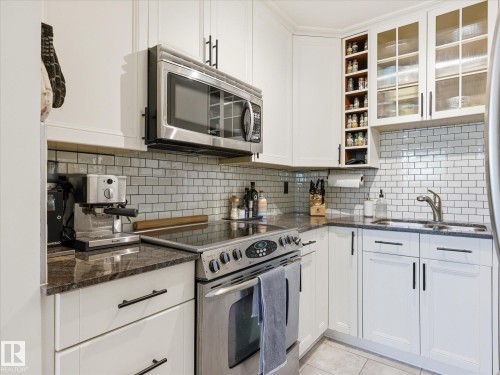 Kitchen featuring white shaker-style cabinetry, granite countertops, stainless steel appliances, a white subway tile backsplash, and frosted glass upper cabinets - 301 10003 87 Avenue, Edmonton, AB - Indoor Photo Showing Kitchen With Double Sink With Upgraded Kitchen