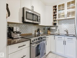 Kitchen featuring white shaker-style cabinetry, granite countertops, stainless steel appliances, a white subway tile backsplash, and frosted glass upper cabinets - 