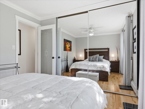 Mirrored sliding closet doors reflecting a bright interior with wood-finish flooring, white crown molding, and a ceiling fan with integrated lighting - 301 10003 87 Avenue, Edmonton, AB - Indoor Photo Showing Bedroom