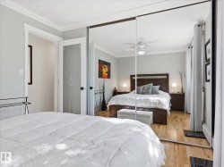 Mirrored sliding closet doors reflecting a bright interior with wood-finish flooring, white crown molding, and a ceiling fan with integrated lighting - 
