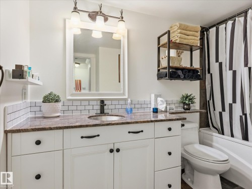 Bathroom vanity featuring white cabinetry, a brown speckled countertop, and subway tile backsplash - 301 10003 87 Avenue, Edmonton, AB - Indoor Photo Showing Bathroom