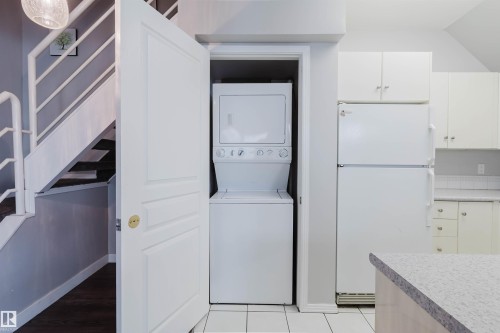 Compact laundry closet with a stacked washer and dryer, white kitchen cabinetry, and a refrigerator - 202 10939 82 Avenue, Edmonton, AB 