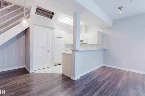 Open concept living area featuring dark wood-finish flooring, a contemporary kitchen with white cabinetry and appliances, and a breakfast bar - 202 10939 82 Avenue, Edmonton, AB 