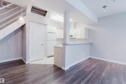 Open concept living area featuring dark wood-finish flooring, a contemporary kitchen with white cabinetry and appliances, and a breakfast bar - 