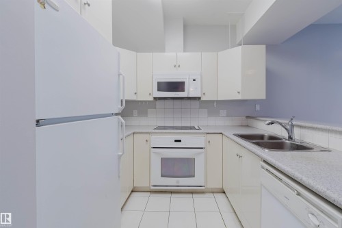 U-shaped kitchen with white cabinetry and appliances, including a built-in microwave, electric cooktop, and oven - 202 10939 82 Avenue, Edmonton, AB 