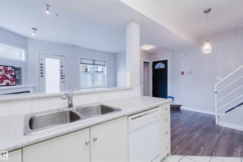 Kitchen with a double basin stainless steel sink, solid surface countertops, and white cabinetry - 202 10939 82 Avenue, Edmonton, AB 