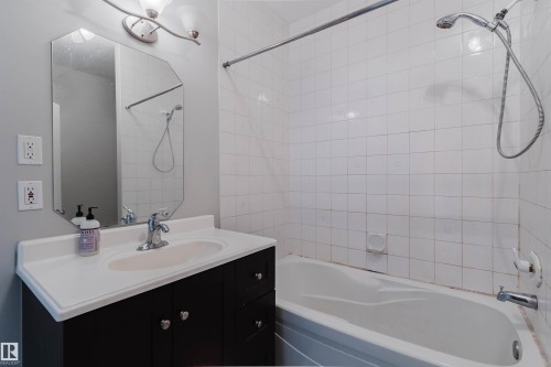 Bathroom featuring a white subway tile shower surround, integrated bathtub, vanity with a built-in sink, dark wood-finish cabinetry, and a chrome faucet - 202 10939 82 Avenue, Edmonton, AB 