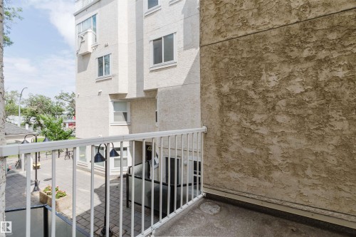 Private outdoor balcony space with white metal railings, concrete flooring, and a textured stucco exterior wall - 202 10939 82 Avenue, Edmonton, AB 