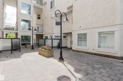 Paved courtyard featuring a textured stucco exterior, multiple balconies with white railings, and integrated planter boxes with flowering plants - 