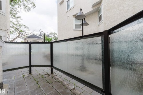 Private patio space featuring textured privacy screens, paver stone flooring, and exterior wall lanterns - 202 10939 82 Avenue, Edmonton, AB 