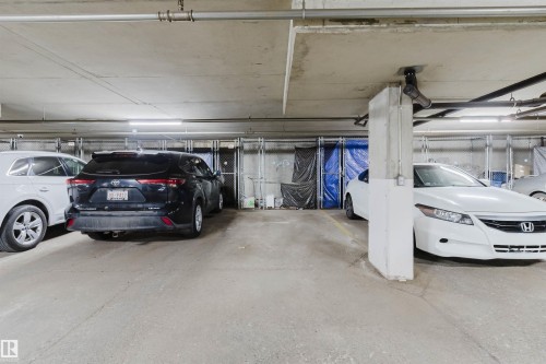 Underground parking garage featuring concrete flooring, exposed overhead piping, fluorescent lighting, and chain link storage units - 202 10939 82 Avenue, Edmonton, AB 